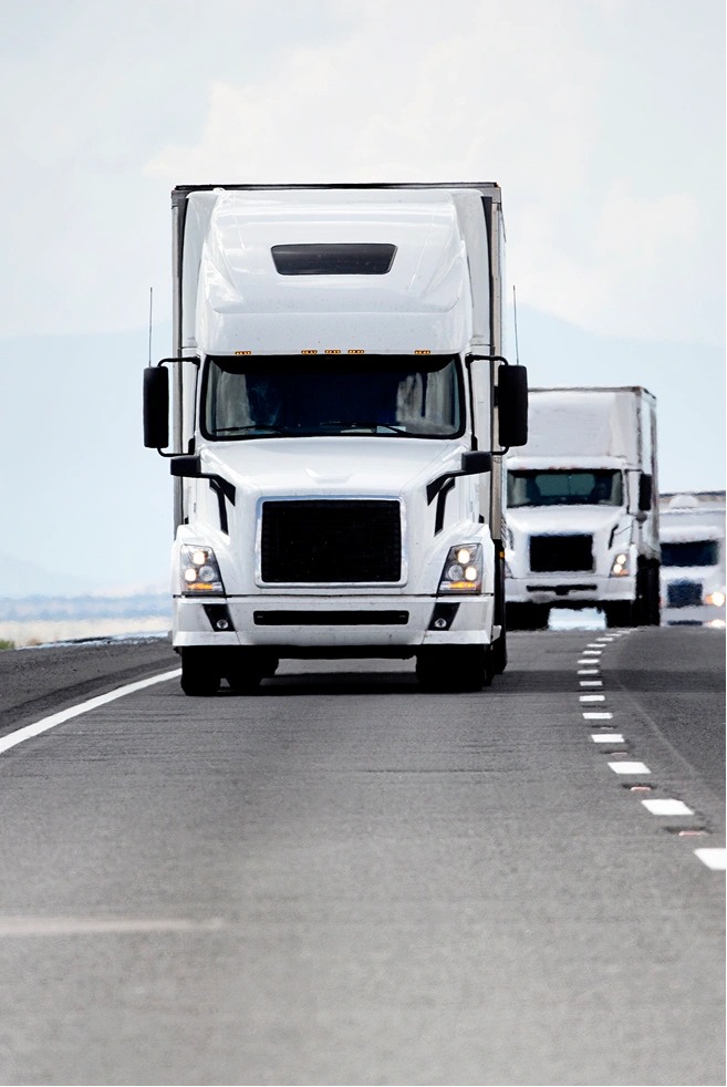 Two white trucks driving on a highway under a cloudy sky
