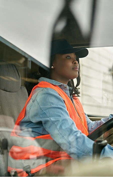 Woman in an orange safety vest driving a vehicle, focused on the road