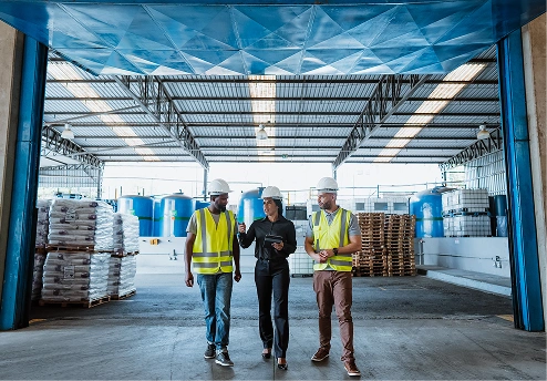Three workers in safety gear discussing in a warehouse with chemical supplies