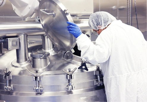 Worker in a lab coat inspecting a large stainless steel chemical tank