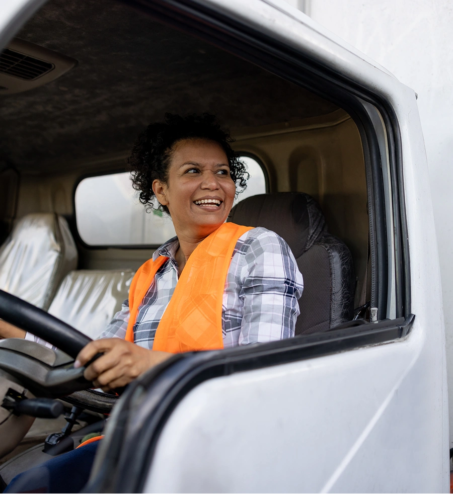 Woman in a truck wearing an orange safety vest, smiling while driving