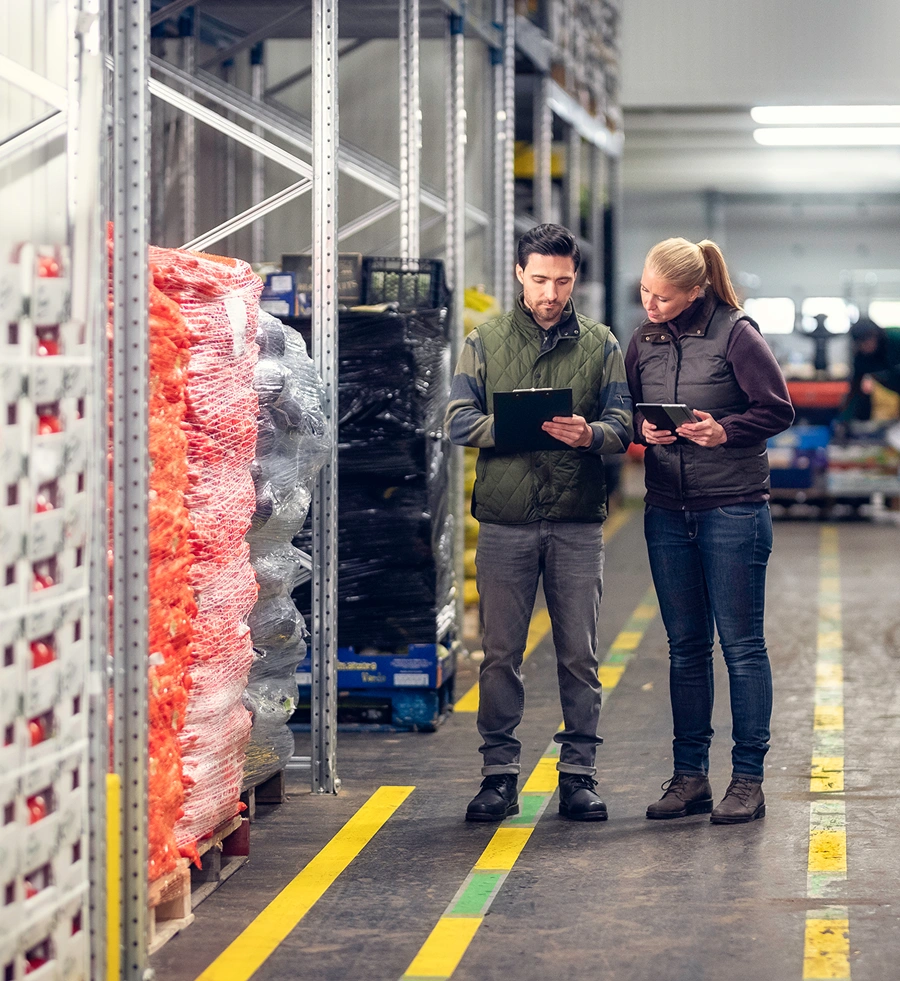 Two warehouse workers reviewing inventory on tablets in a storage facility