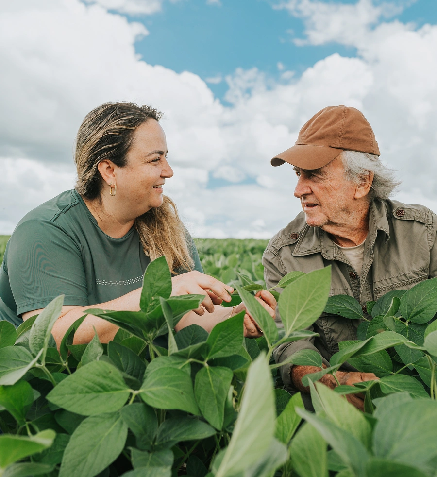 Two people discussing crops in a green field under a blue sky