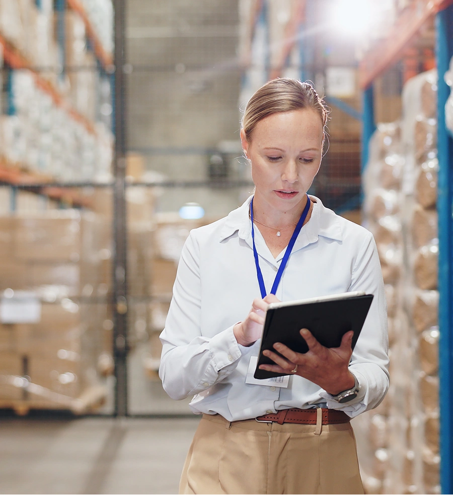 Woman in a warehouse using a tablet, surrounded by stacked boxes