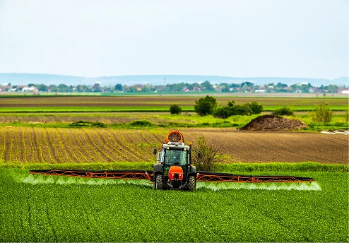 Tractor spraying pesticides in a lush green agricultural field