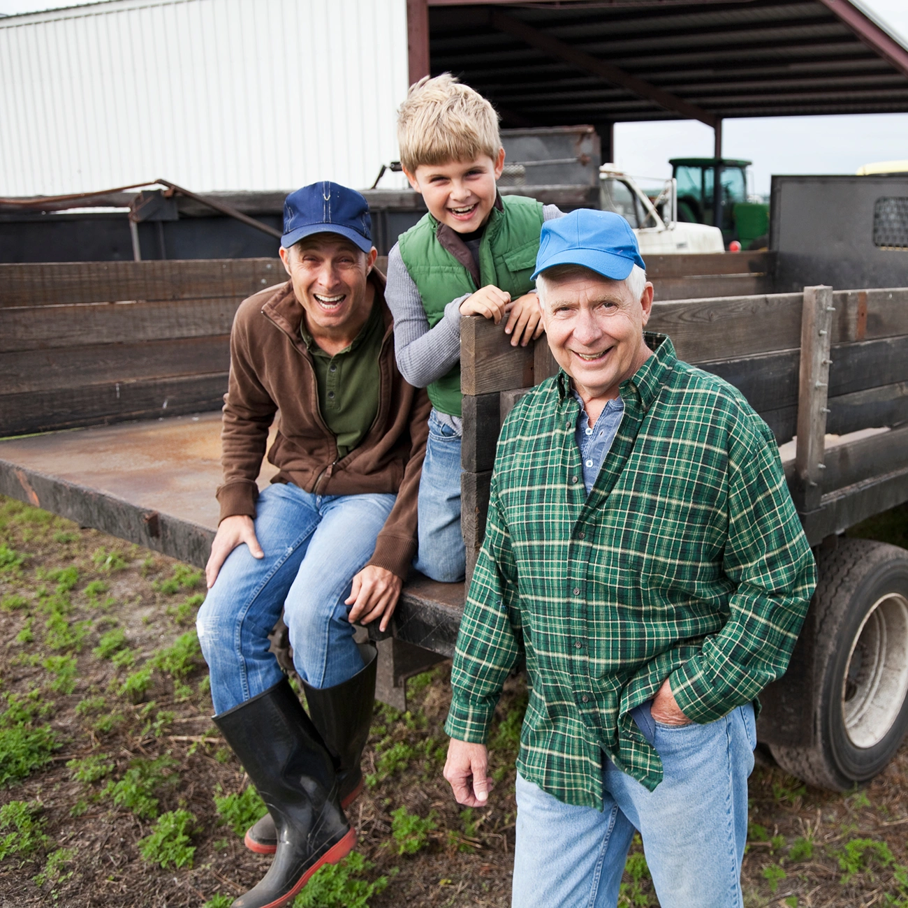 Three men, including a boy, smiling on a farm truck in a rural setting