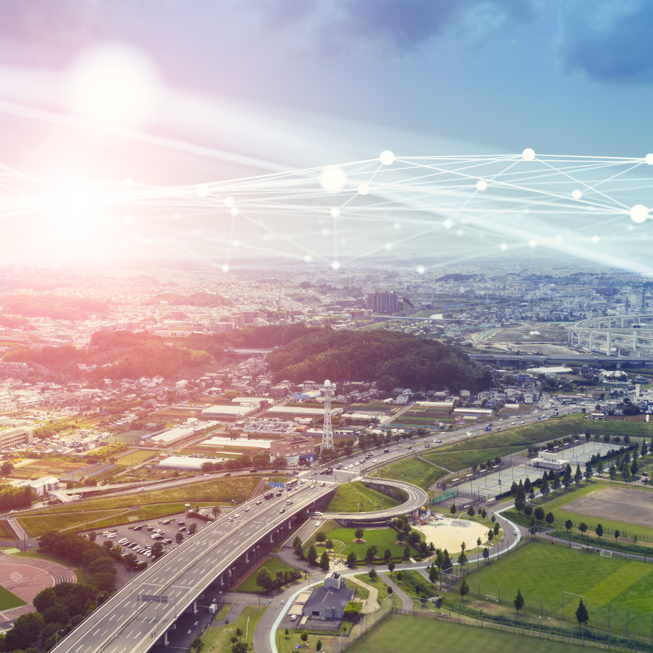 Aerial view of a cityscape with highways and green fields under a bright sky