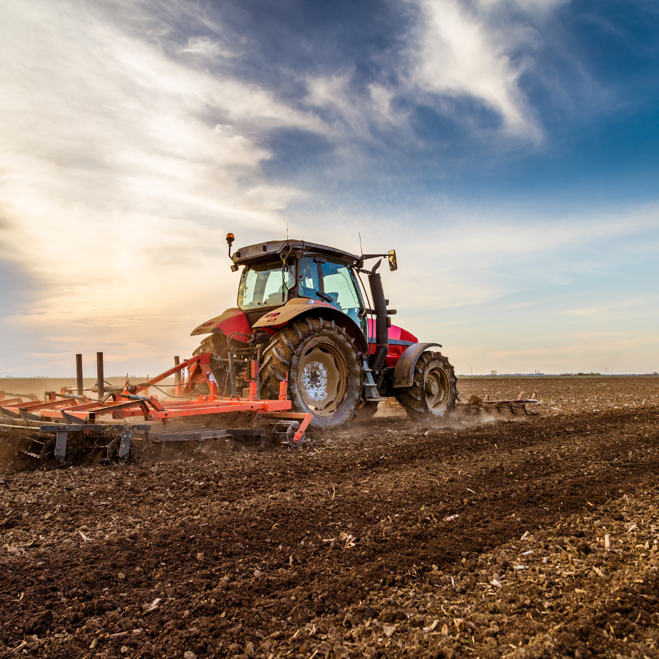 Tractor plowing a field at sunset with a blue sky