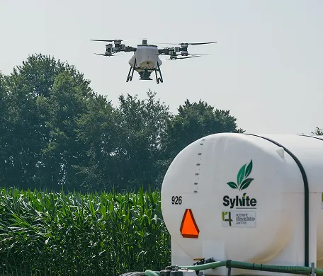 Agricultural drone flying beside a Sylvite tank in a field