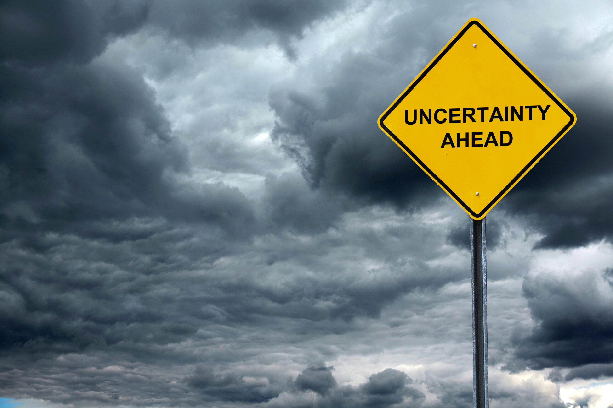 road warning sign with text uncertain ahead in front of storm cloud background road warning sign with text uncertain ahead in front of storm cloud background