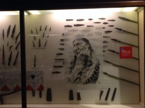 Chris Pappan's "Thank You, Grandmother" layered atop a display case of speers and speerheads.