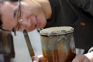 Yuxin Zhou looking at a sediment core, holding a metal spatula.