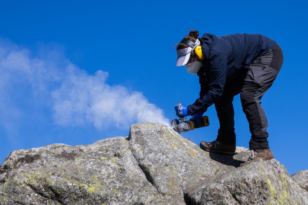 Helen Dulfer uses an angle grinder to cut into a boulder April 10 in Ireland’s Wicklow Mountains. She carved perpendicular lines into the rock before using a chisel to fully remove the rock sample. (Cathy Ching / Medill)