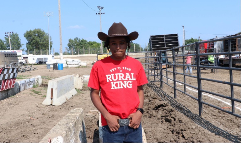 Young man stands in rodeo arena.