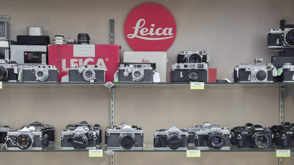 Rows of Leica, Nikon and Canon compact cameras in a camera store.