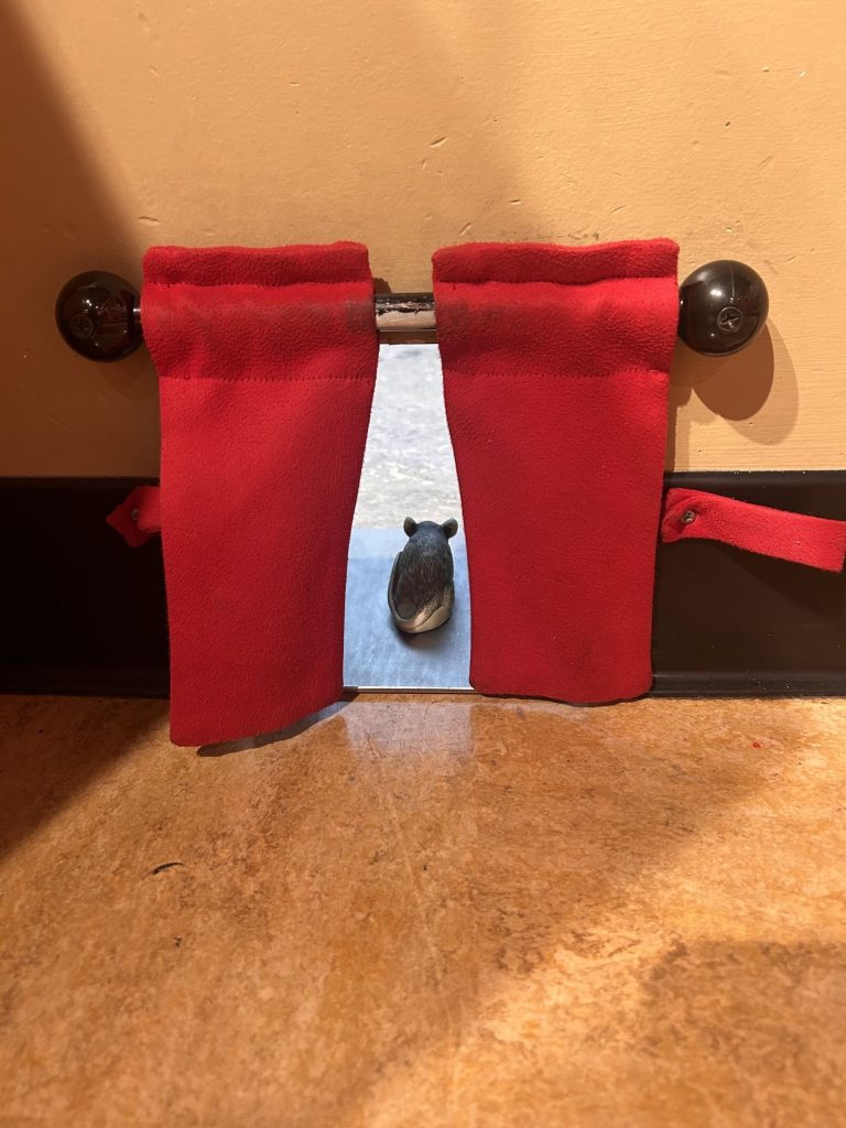 Toy mouse peeking through red curtains