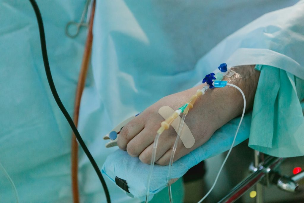 Patient's arm with IV drip in a blue hospital gown.