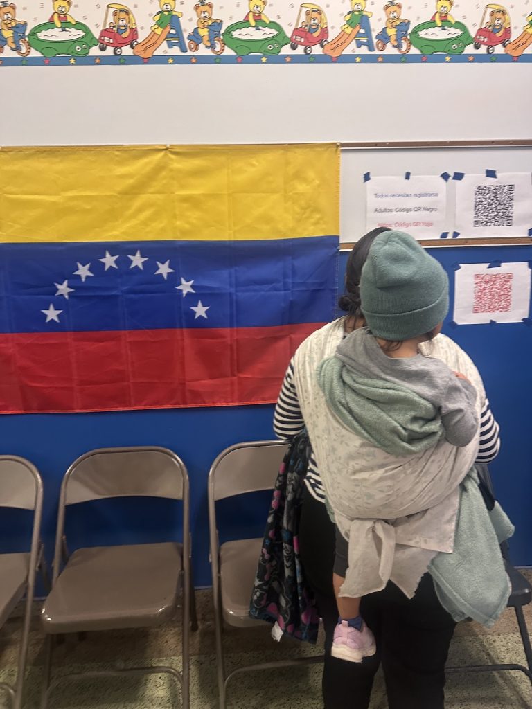 Woman carrying child in front of Venezuela flag