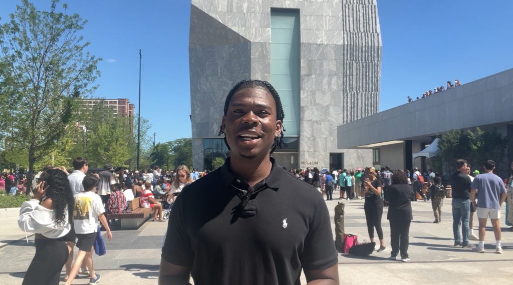 Man smiling in front of Barack Obama center, crowd in background