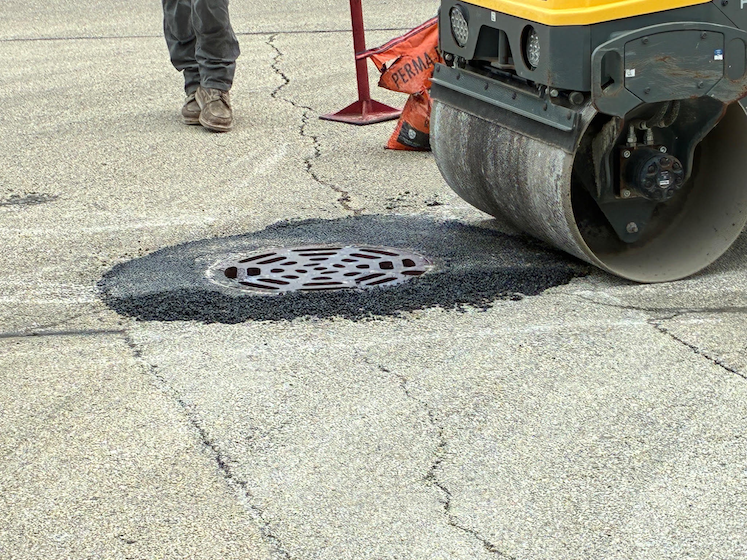 Road roller compacting asphalt around manhole