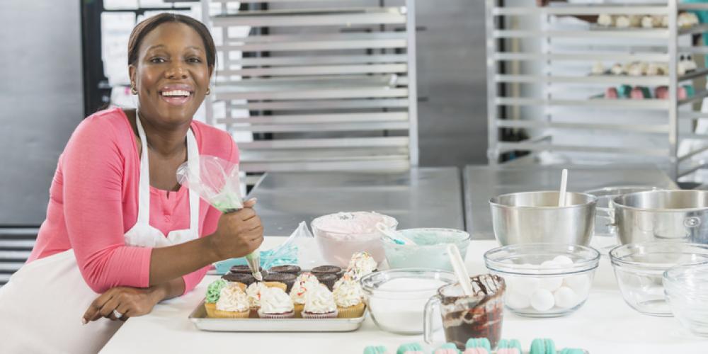 Female baker smiling as she ices cupakes in kitchen