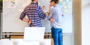 Woman and man discussing about business strategy using whiteboard.