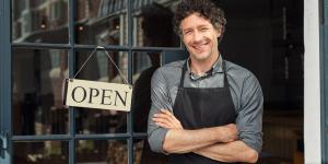 Small business owner Male small business owner standing outside of store with open sign smiling
