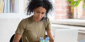 African woman working with laptop making notes