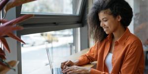 Happy African American woman copywriter working freelance project in modern cafe.