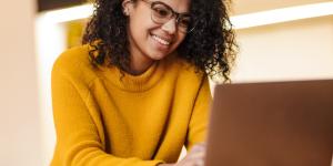 cheerful african american woman in eyeglasses using laptop