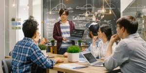 Charismatic Asian Team Leader Shows Laptop with Data Statistics to Diverse Group of Talented Young Developers