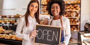 Two female business owners hold open sign in bakery