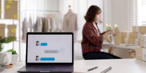 Female, Asian small business owner works in background while chatbot on computer answers customer question
