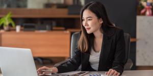 Asian businesswoman analyzes charts using laptop calculator at the office