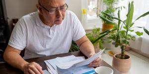 A senior man sitting by a table calculating the raising cost of energy and tax bills.