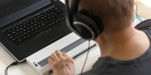 Blind person working on computer with braille display and screen