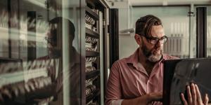 Who Can Help to Prevent Future Ransomware Attacks bearded man in pink shirt holding laptop standing next to server tower
