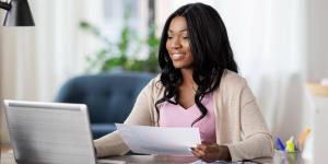 happy smiling african american young woman with laptop computer and papers working at home office