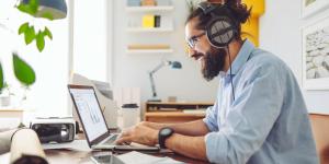 Man using laptop to look at resources Man wearing headphones and glasses smiling as he uses his laptop