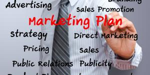 Photo of a businessman writing 'Marketing Plan' on a glass board, along with other marketing terms