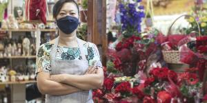 Steps to Help Small AAPI Business Owners asian woman stands in flower shop wearing a light color floral shirt surrounded by red flowers
