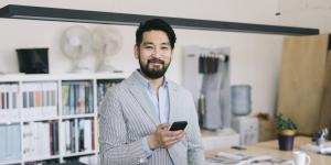 Thriving as an AAPI Business Owner: Common Challenges and Solutions asian man smiling in office wearing striped blazer and holding phone