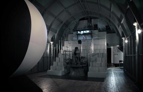 <p>Lindsay Seers. Nowhere Less Now | An Artangel Project | 8 September - 21 October 2012. Seating rack. Materials: Wood, cardboard, scaffolding poles, polystyrene, dexion, HD video projection, headphones.</p>