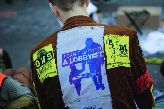 An image of the back a person wearing a jacket. A patch on the jacket reads “I can’t afford a lobbyist”.