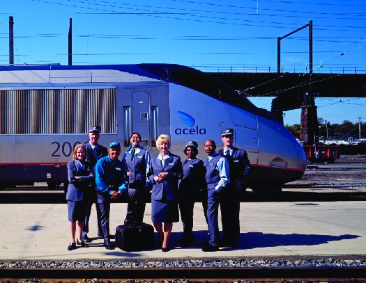 A photo of Amtrak staff standing on a train platform as a train passes behind them.