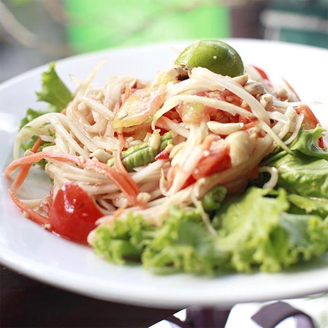 Vegan Som Tam, or papaya salad, served on a white plate with garnish.