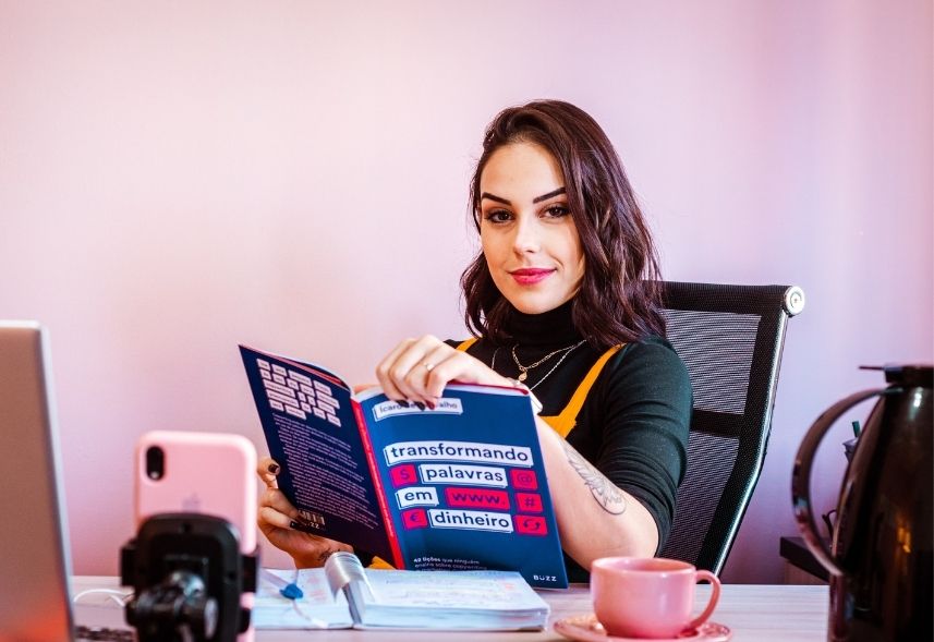 influenciadores digitais: imagem de uma mulher sentada em uma cadeira folheando uma revista com um celular gravando a imagem