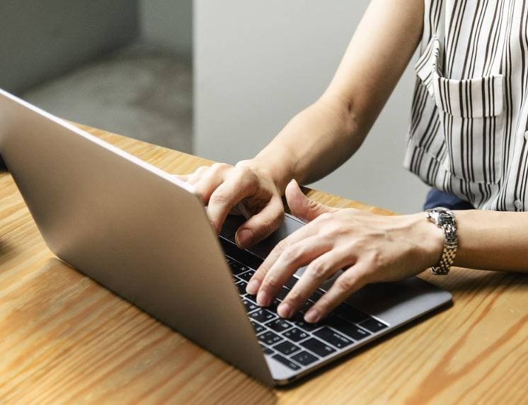 Marketing de Conteúdo: imagem das mãos de uma mulher digitando no notebook apoiado em cima da mesa.