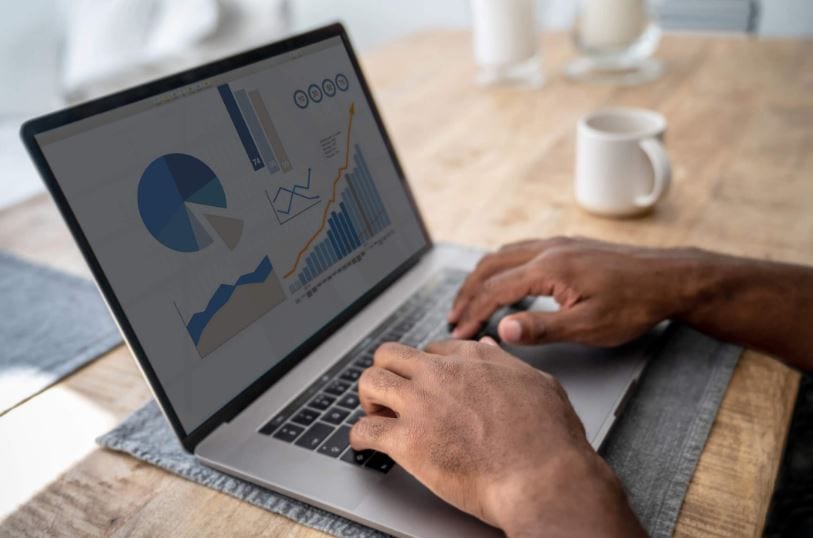 Como criar conta no Google Analytics: imagem das mãos de um homem digitando em um notebook apoiado em uma mesa de madeira com uma caneca de café ao lado.