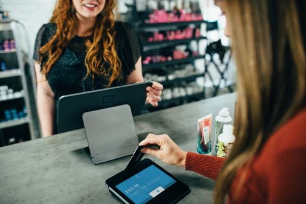 Jornada de compra: imagem de duas mulheres em uma loja. Uma é a vendedora que está passando o cartão da cliente para efetuar o pagamento.